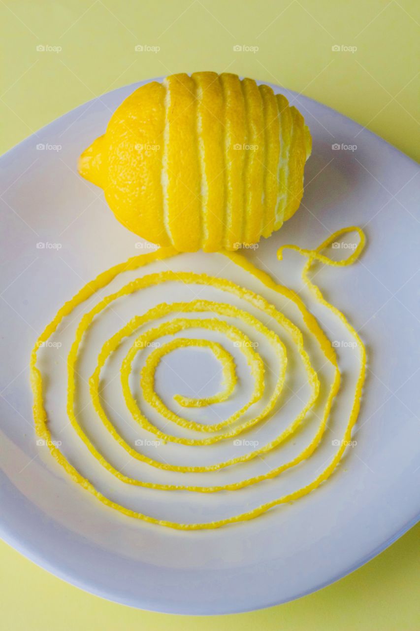 Lemon and spiraled lemon peel on a white plate with yellow background  