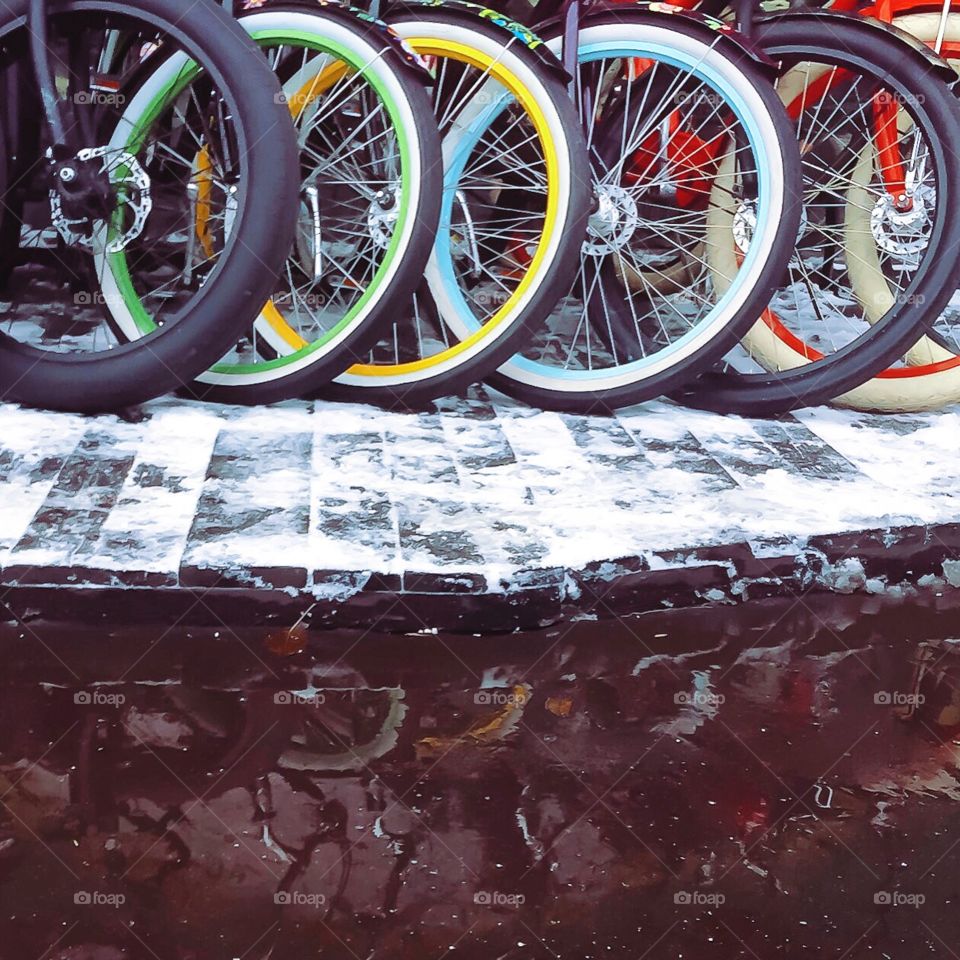 Multicolored bicycle weeks on snow-covered pavement and their reflection in a puddle