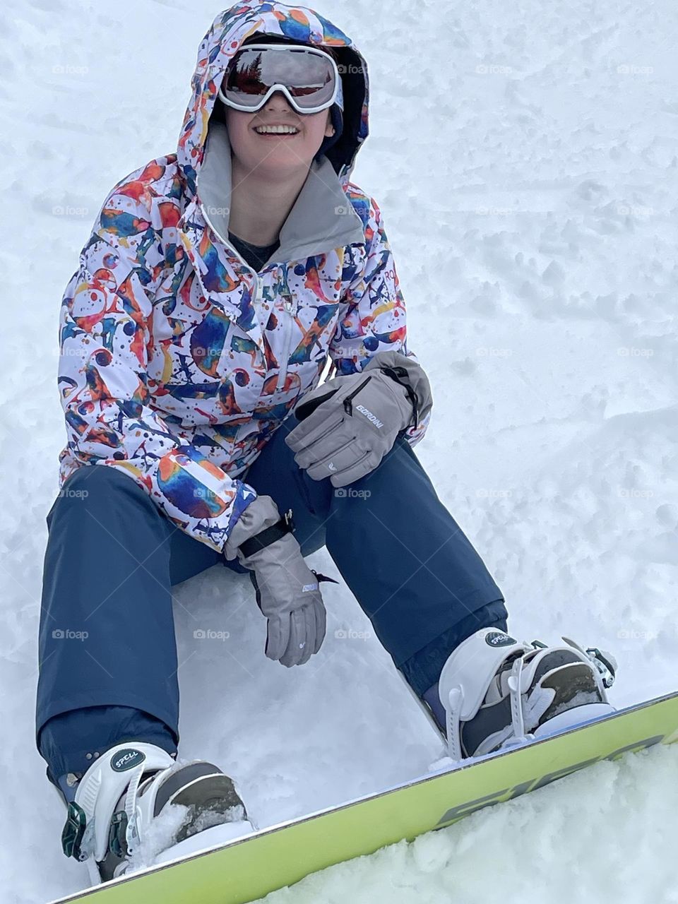 A young female snowboarder takes a well deserved break from the action of the mountain on a clear day with fresh powder