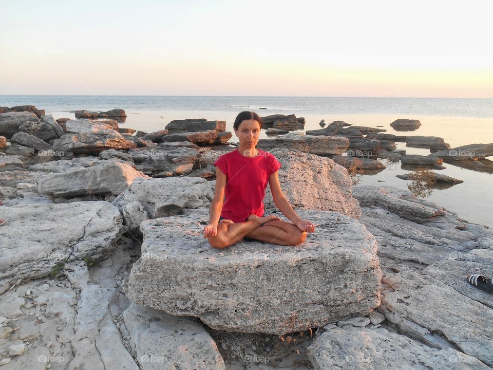 girl training yoga lotus meditation on a sunset sea stones shore summer time