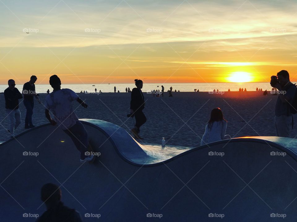 Venice Beach Skatepark with skateboarders riding a bowl during a peaceful golden hour sunset on the beach next to the Pacific Ocean. 
