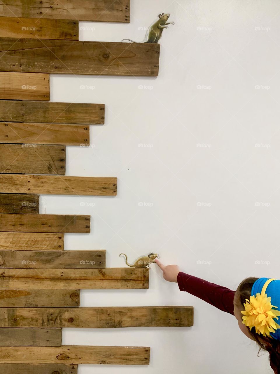 Summer girl child playing with the wall mouse decoration in a creamery with realistic looking as if the mice were truly standing and interacting on wood planks with her with a blue head covering and yellow large flower head band.