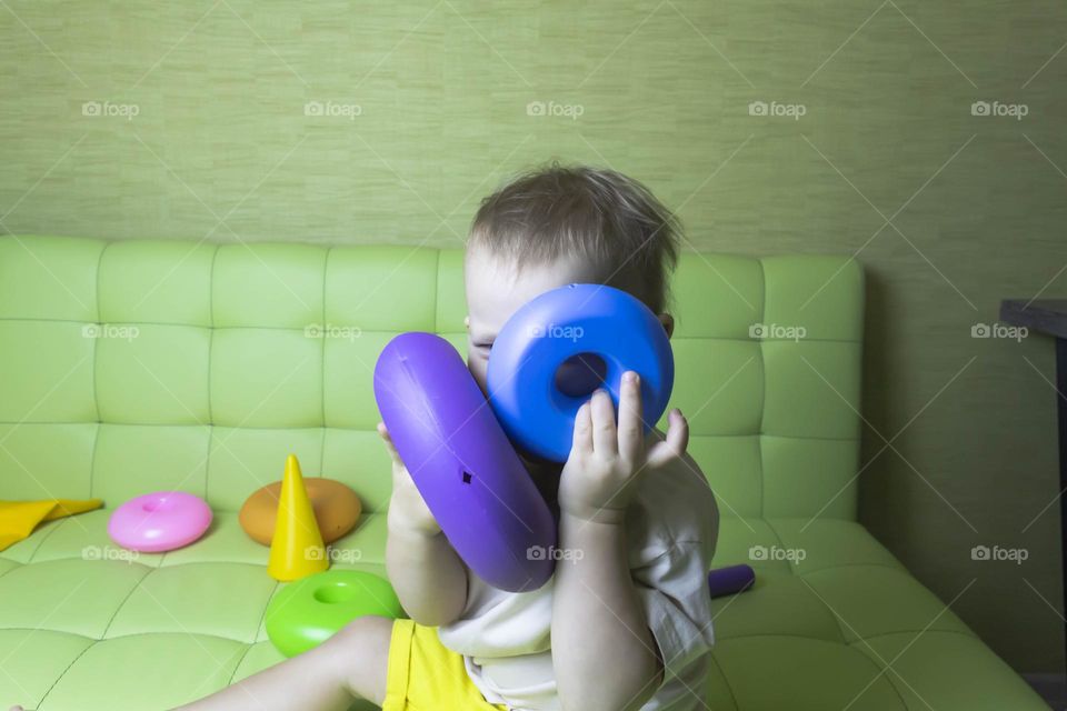 The child is having fun playing a bright pyramid educational toy, sitting on a green sofa.