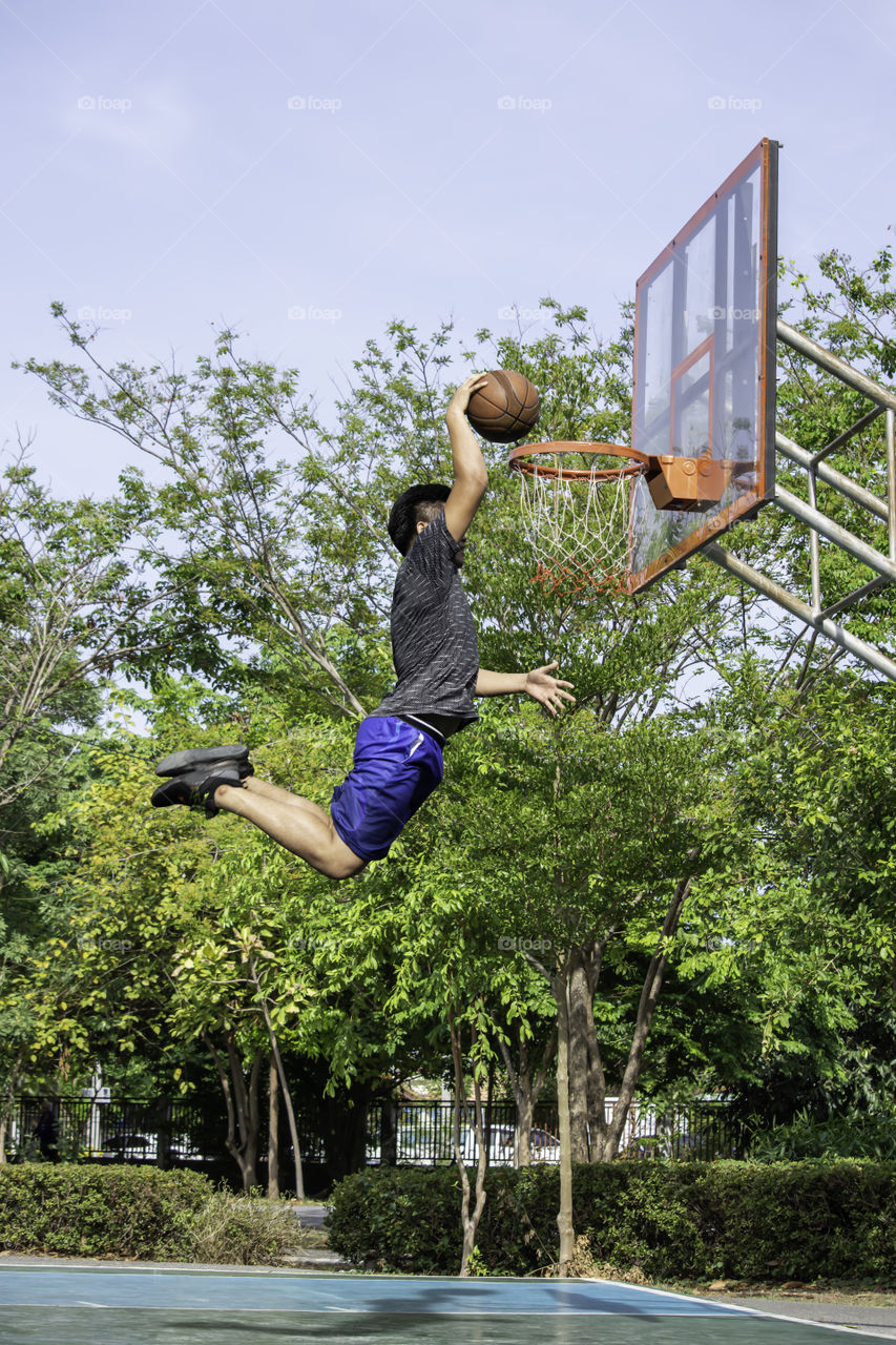 Basketball in hand man jumping Throw a basketball hoop Background  tree in park.