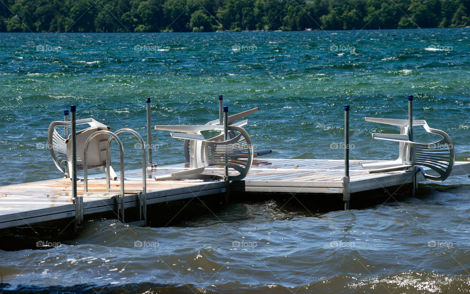 Chairs on dock protected from being blown by wind and storms on turquoise and blue clear water lake conceptual safety and liability insurance symmetric background image