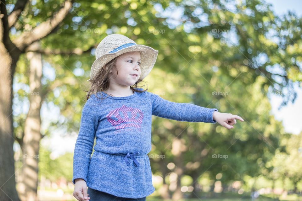 A little girl standing against trees and pointing