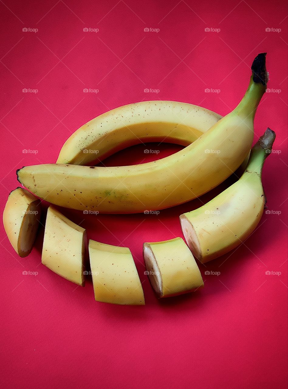 two whole bananas, one banana, sliced.  Red background