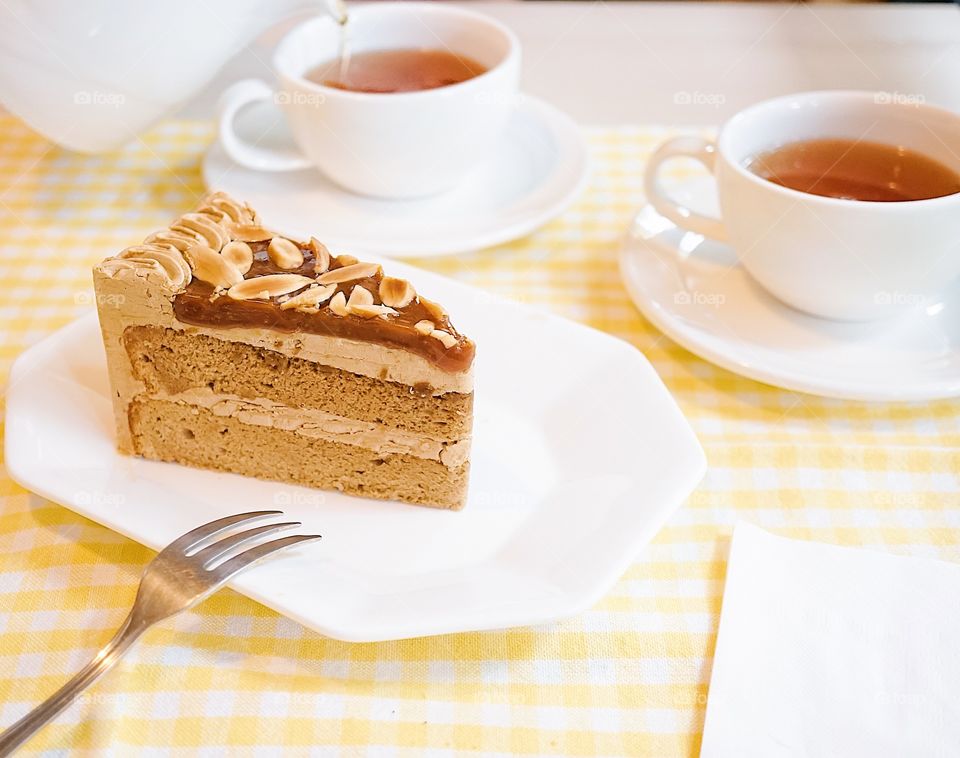 Afternoon tea. Sea salt caramel almond coffee cake serves with cup of teas. Blurred teapot is pouring tea on the background.