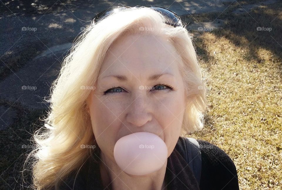 Blond woman blowing a bubble gum bubble outside