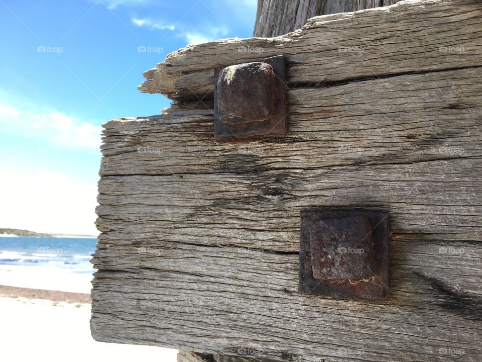 100 year old wood post attached to old abandoned wharf dock at ocean, rusted bolts/stakes 