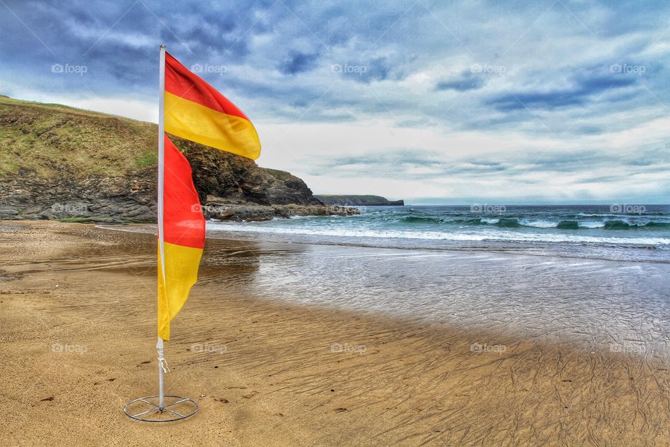 A lifeguards yellow and red warning flag on a deserted sandy beach in Cornwall.