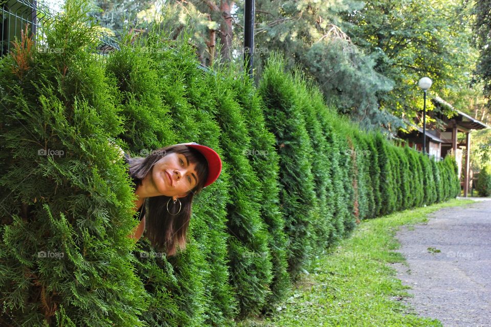 a girl in a red cap peeks out from behind a tree