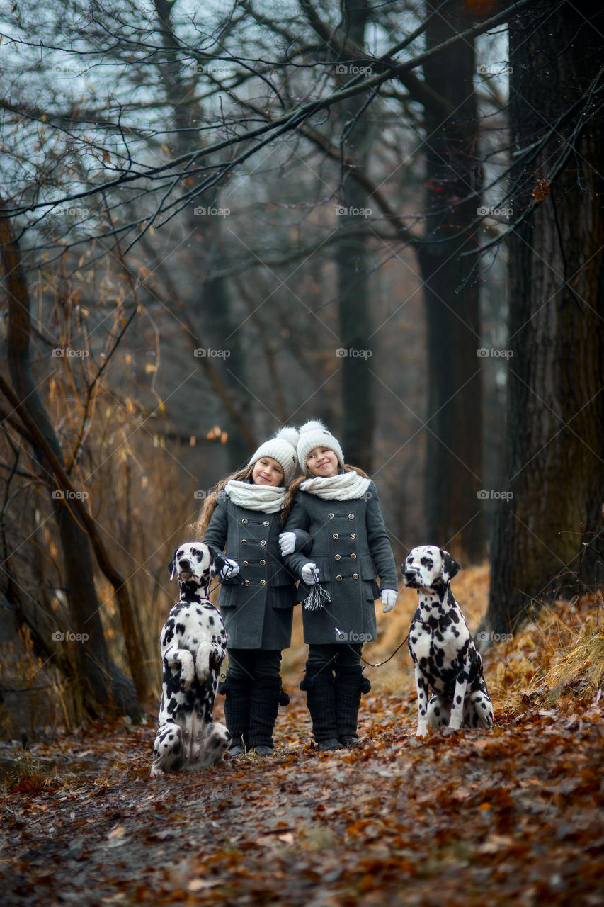 Twins girls with Dalmatian dogs in autumn park 