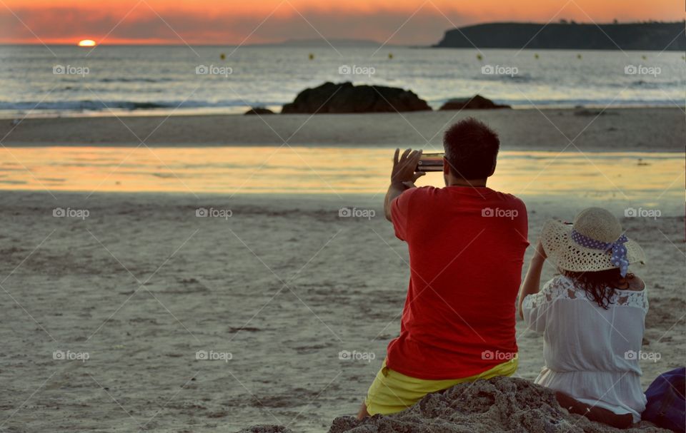 Rear view of couple taking photography of sunset at beach