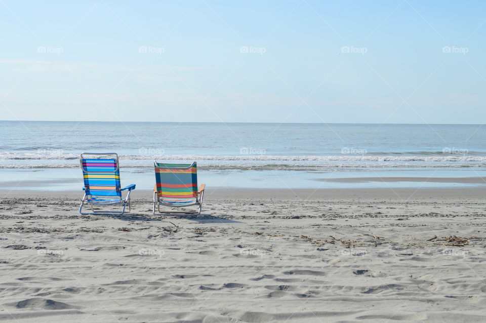 Two empty lounge chairs on the shore of a beach