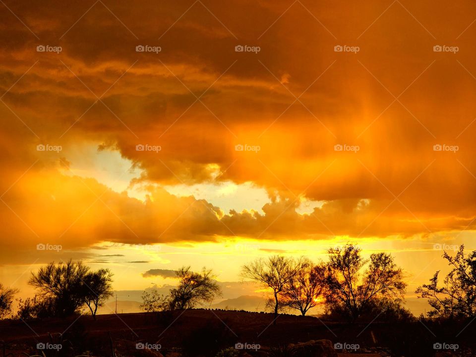 Falling rain and dense cloud cover glow in brilliant orange hues as the sun sets in Arizona