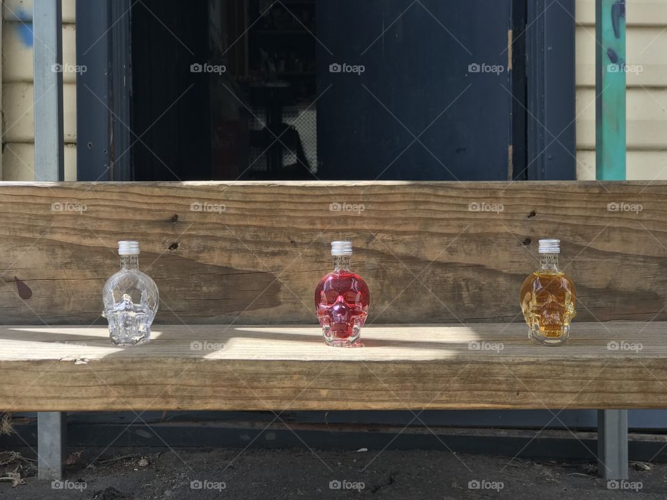 Three small skull bottles of a drink lined up, somewhat spread apart with Sunlight beaming down in the middle. 
