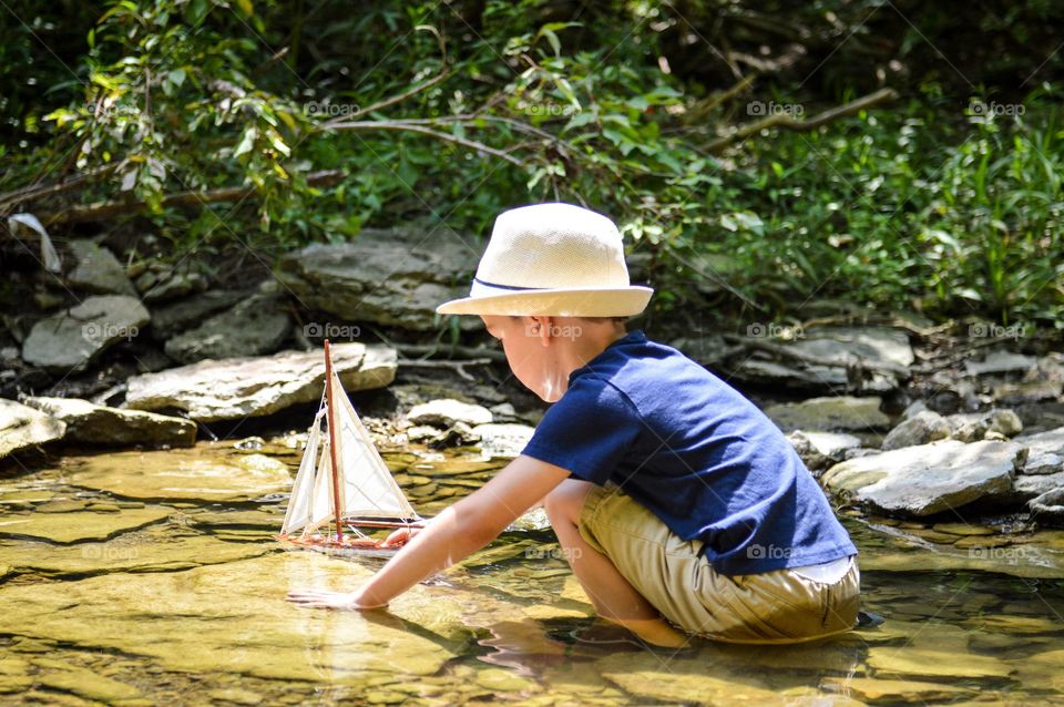 Portrait of a young boy playing with a wooden boat in a creek on a sunny summer day