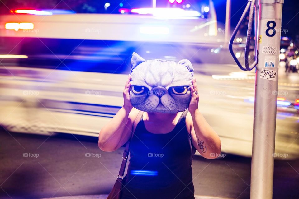 A tattooed woman holding a cat pillow. Bright city lights in the background. Cool urban scene