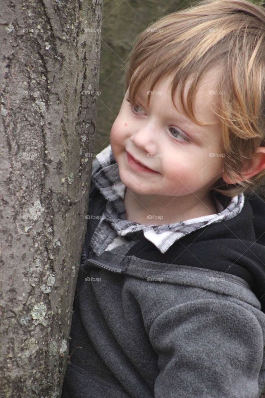 Little boy standing near tree trunk