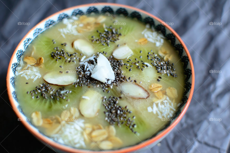 Green and white sweet fruit smoothie bowl isolated closeup of fresh fruit and nuts and healthy ingredient garnish in mandala style design with almond, dark chia seed, coconut and oatmeal 