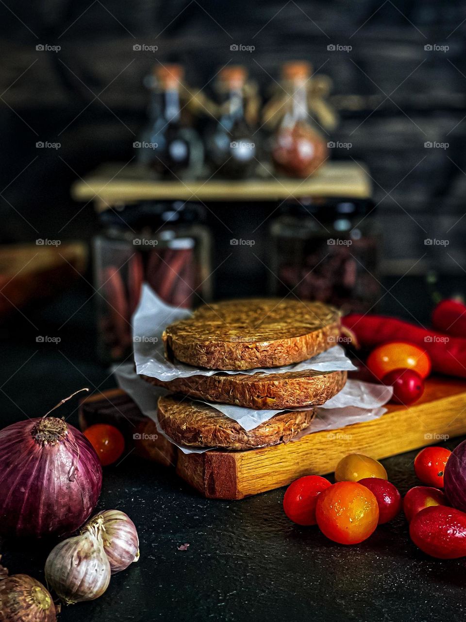 Plant-based burger patties on a wooden board with some vegetables around it and some spices in a jar preparation for cooking