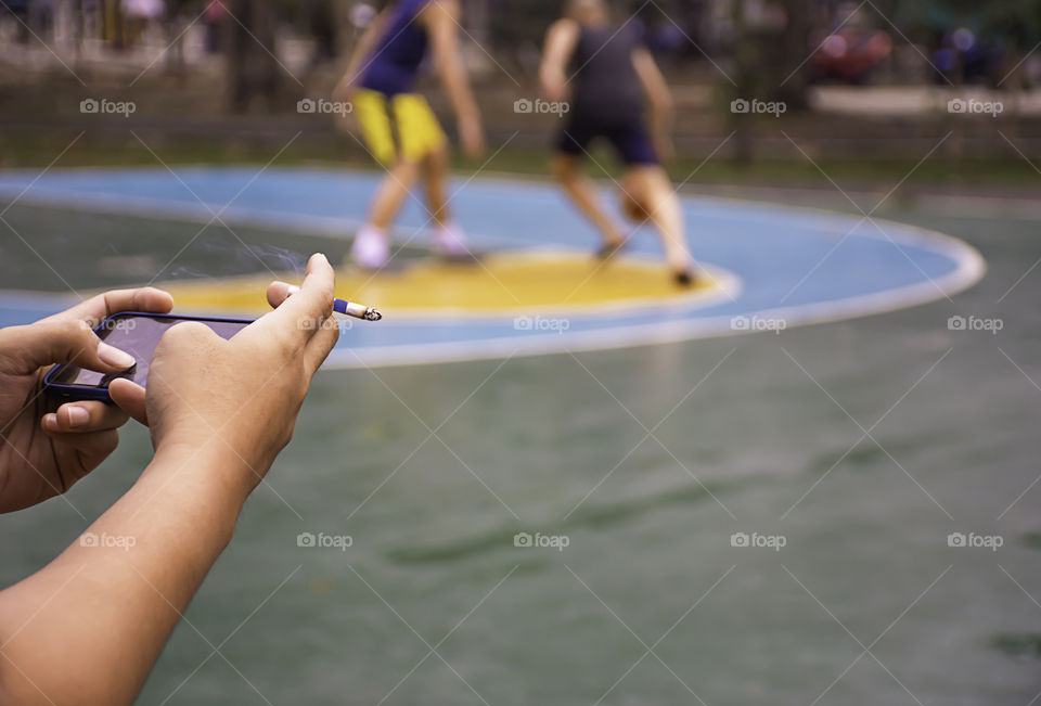 Hand holding a cigarette and a telephone. Background on basketball court