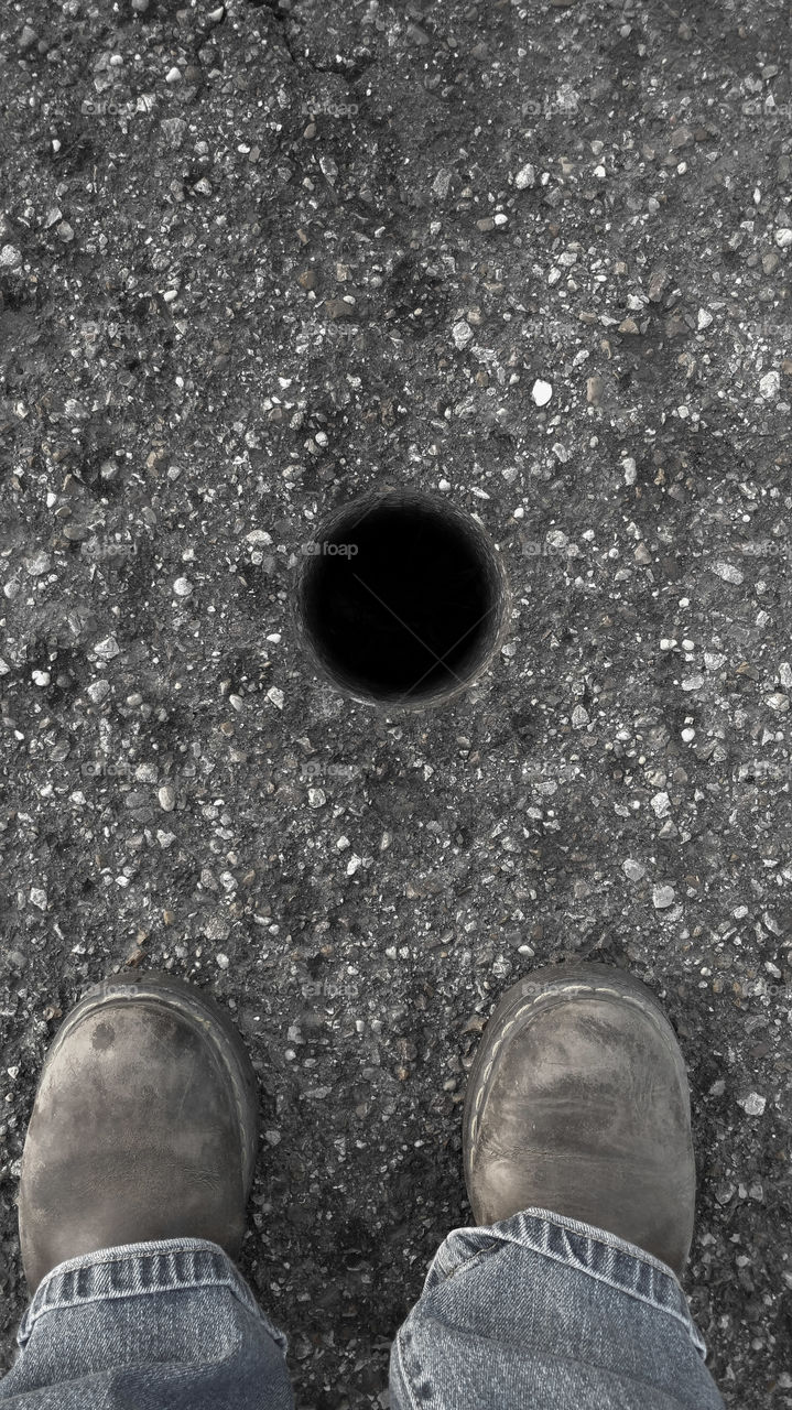 Low section of person standing near hole on street