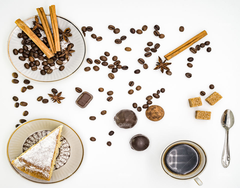 cup of coffee, sweets and different ingredients in plates stand on a white background