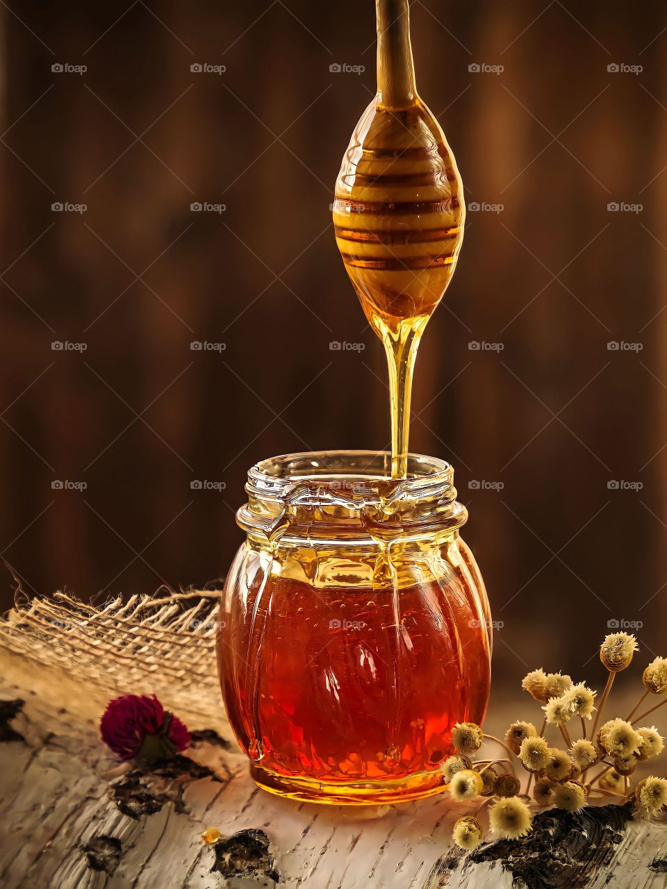 Honey dripping from dripper into the glass jar on blurred background