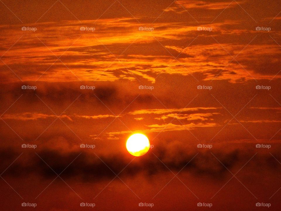 A reddish orange sunrise where it looks like the sun is resting on top of dark clouds at Cranes Roost Park in Altamonte Springs, Florida.