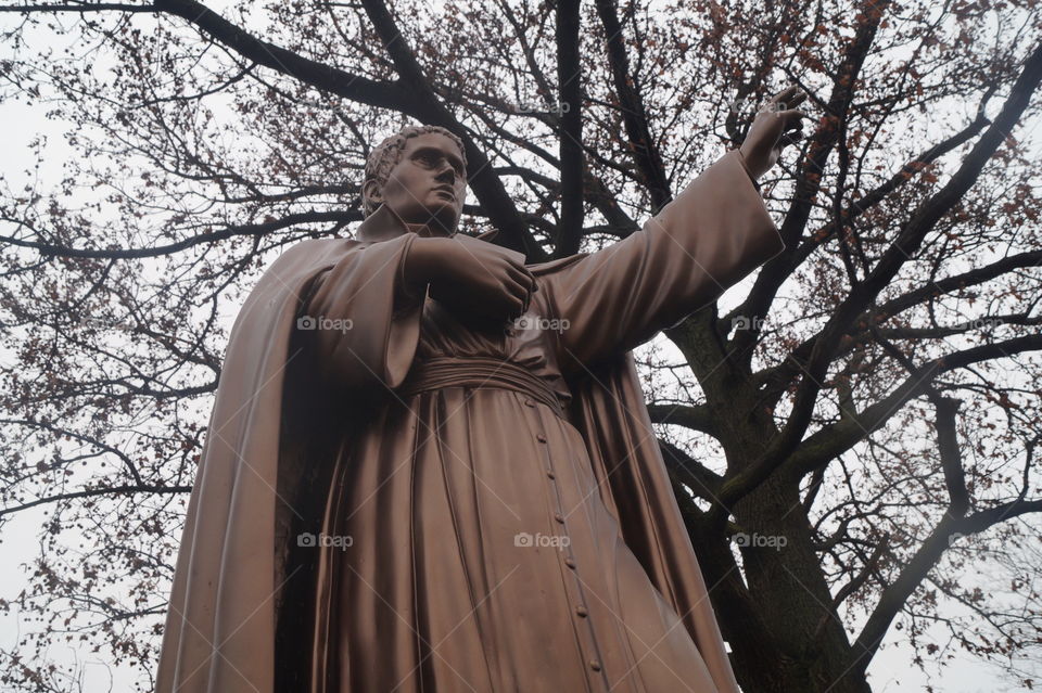 Beautiful photograph of a statue of a Jesuit priest . It appears that he is pointing to God and Heaven. 