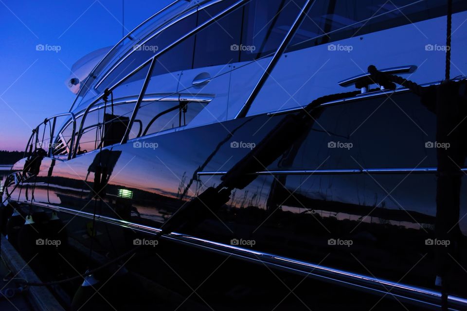 Yacht in marina after sunset. Yacht at the marina captured during a blue hour with setting sun coloring the horizon and reflection of an another boat.