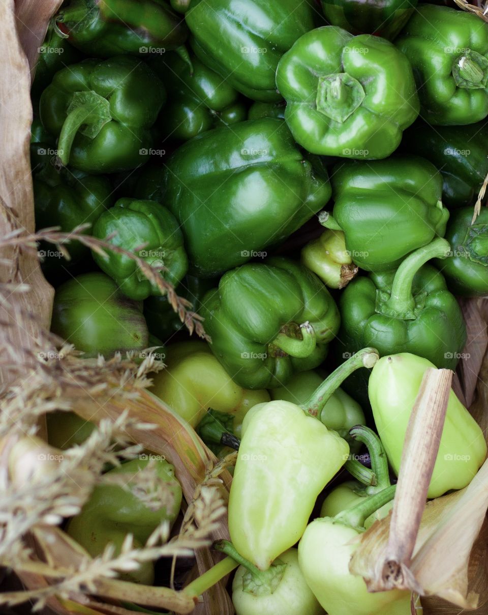 Green homegrown pepper is laying in a box with dried leaves, vitamins and vegetables 