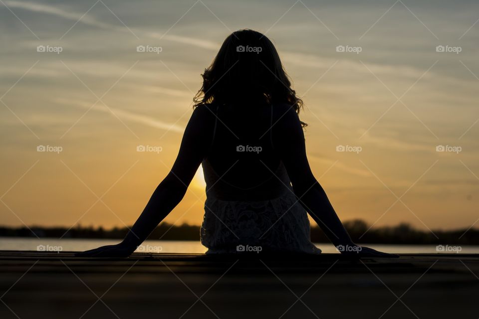 woman slihouette at sunset. woman sitting on a deck at lake enjoying sunset,photo taken from behind,silhouette effect