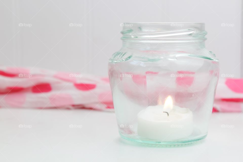 A tea light in a glass jar on a white shelf 