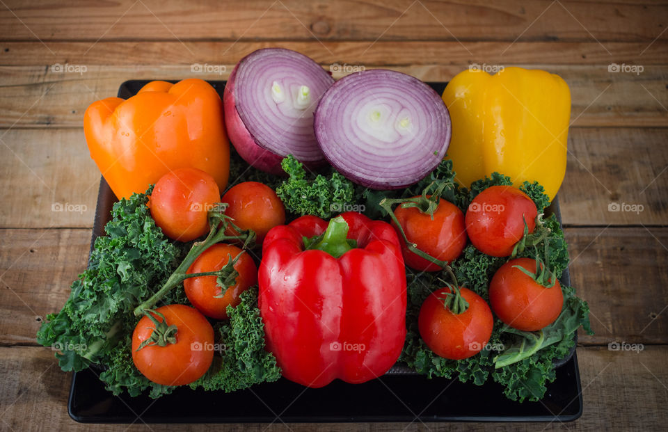 colorful plate of fresh vegetables including red, yellow, and orange peppers, cherry tomatoes, red  onion, and kale on a wood table