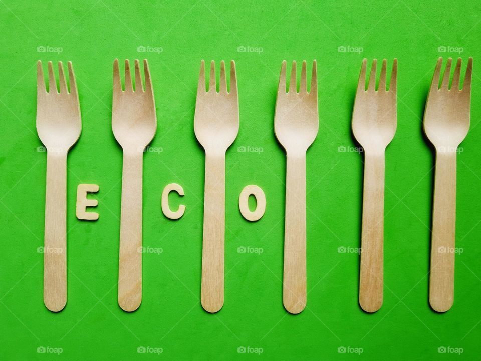 wooden cutlery placed on a green background with eco inscription