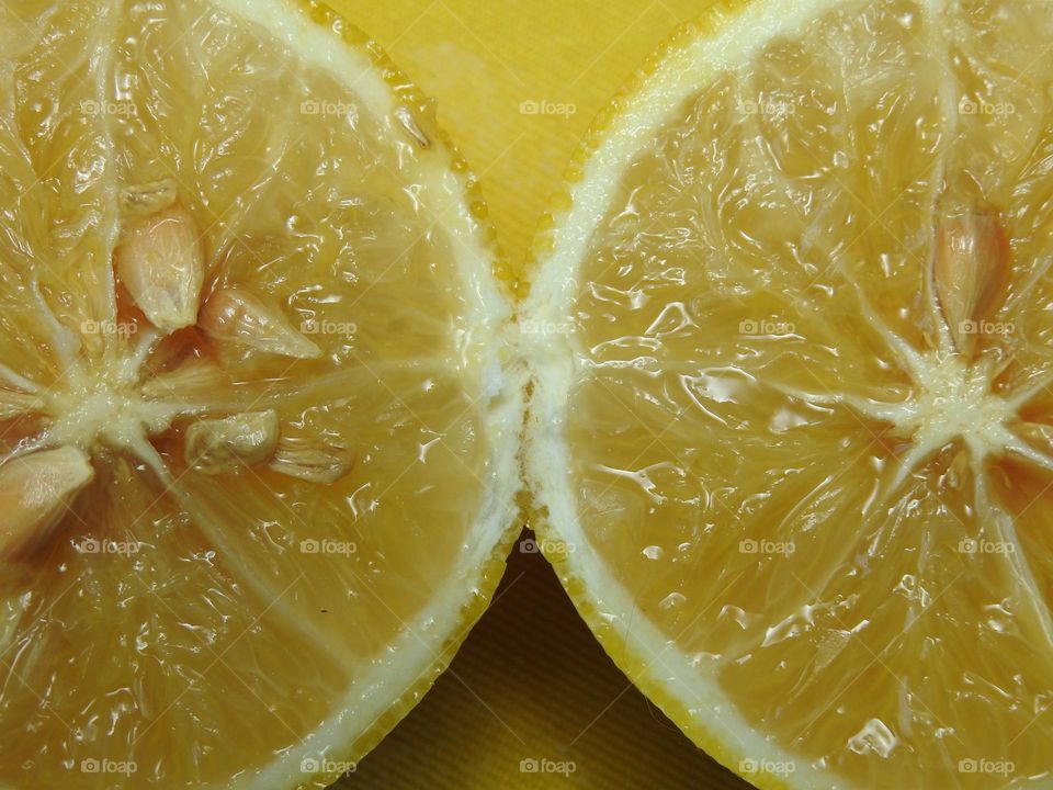 Two lemons with vibrant yellow as a theme with macro closeup on the juicy sliced part and the seeds on top of a yellow apron.