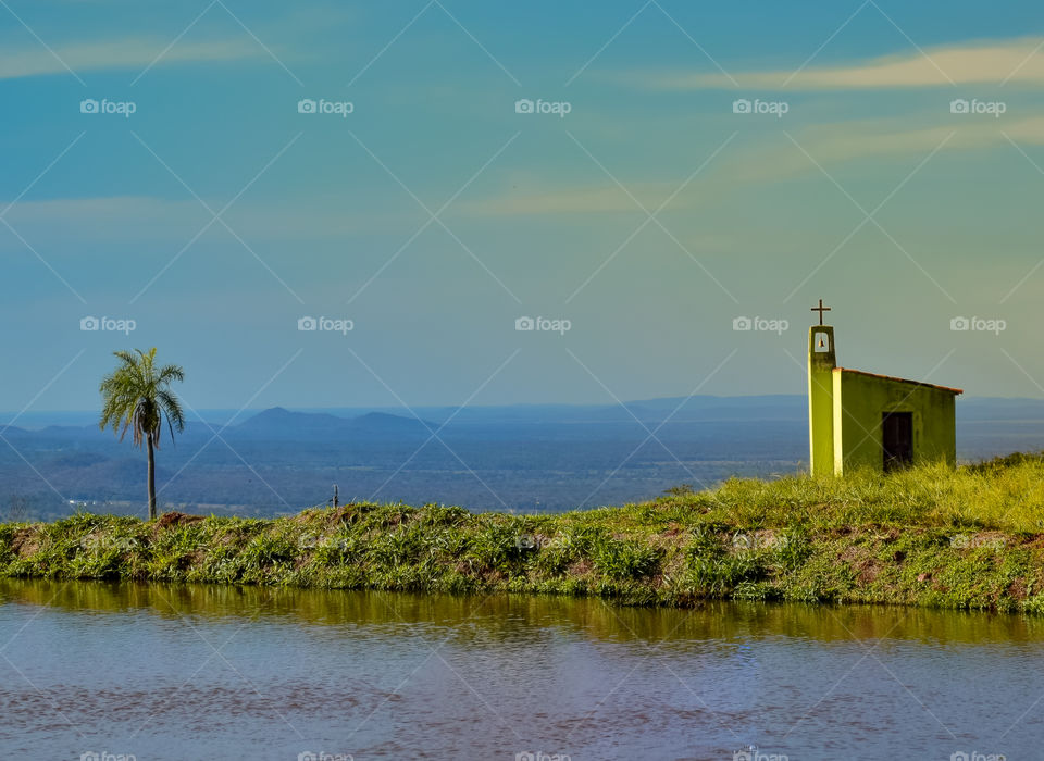 Paisagem com lago e uma pequena capela verde no alto do morro