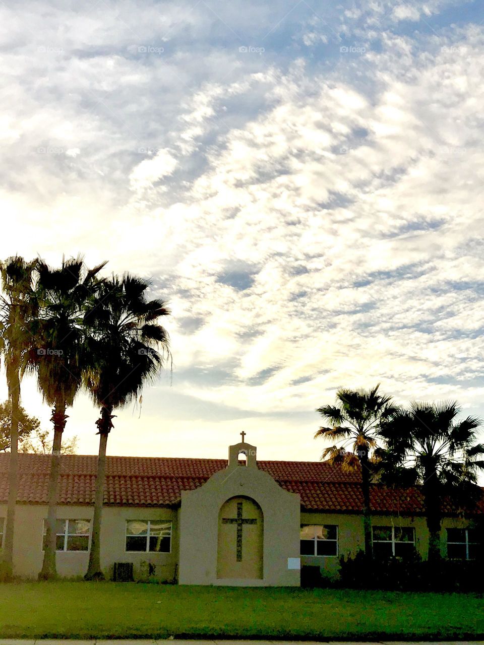 A chapel framing by palm trees under a cloud sky.