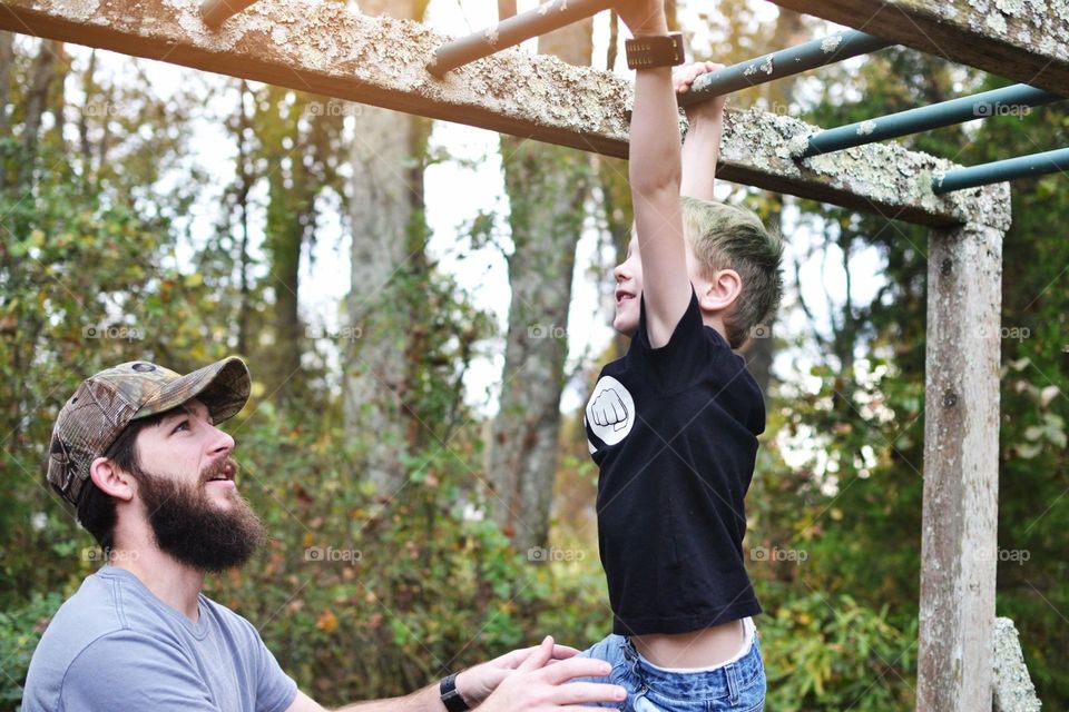 A dad helping his son go across monkey bars. 