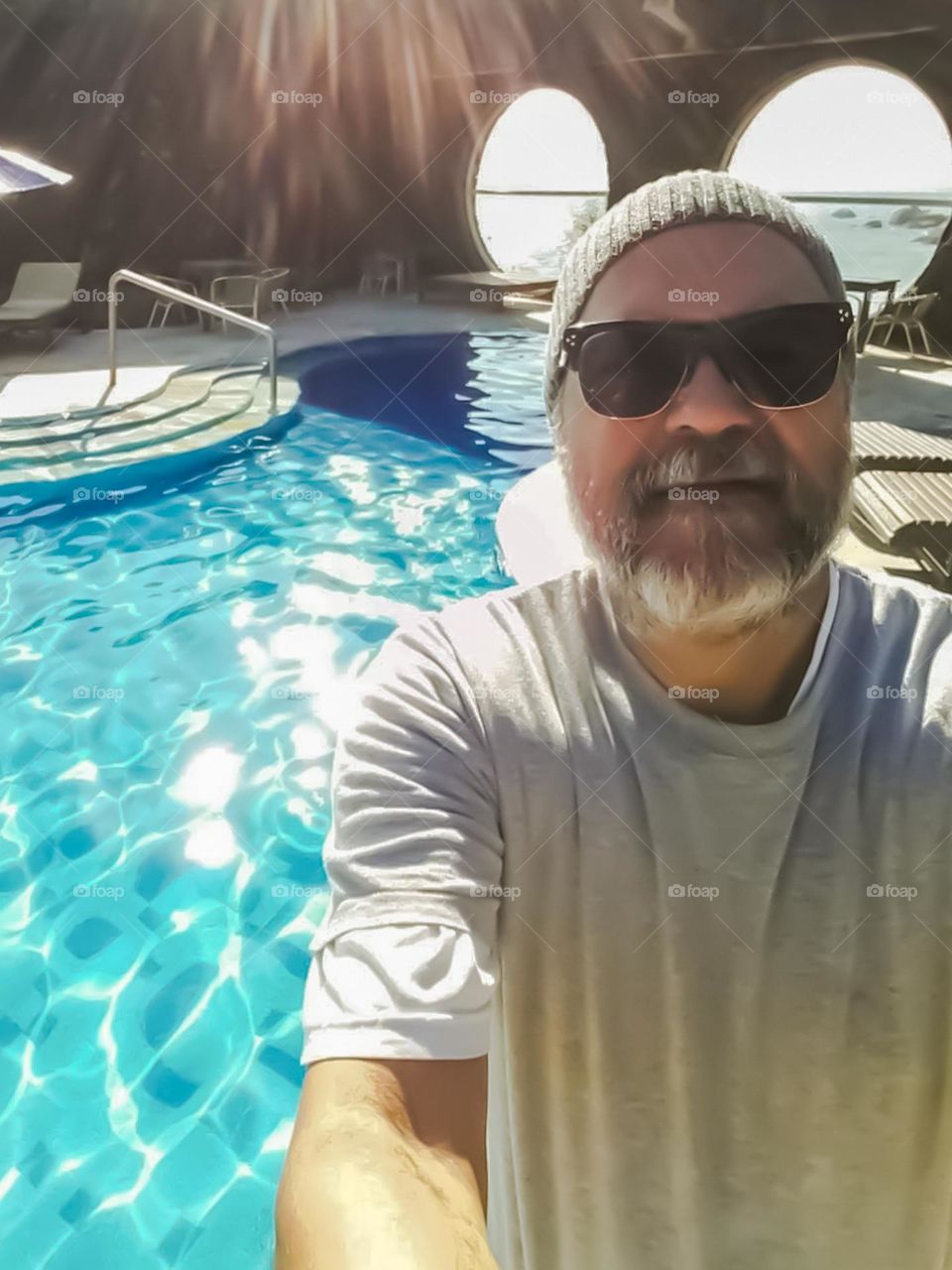 Image of the swimming pool of a Hotel in the Ilhabela Archipelago, with reflection of the sun's rays in and around the water.  In the background the sea that bathes the island.