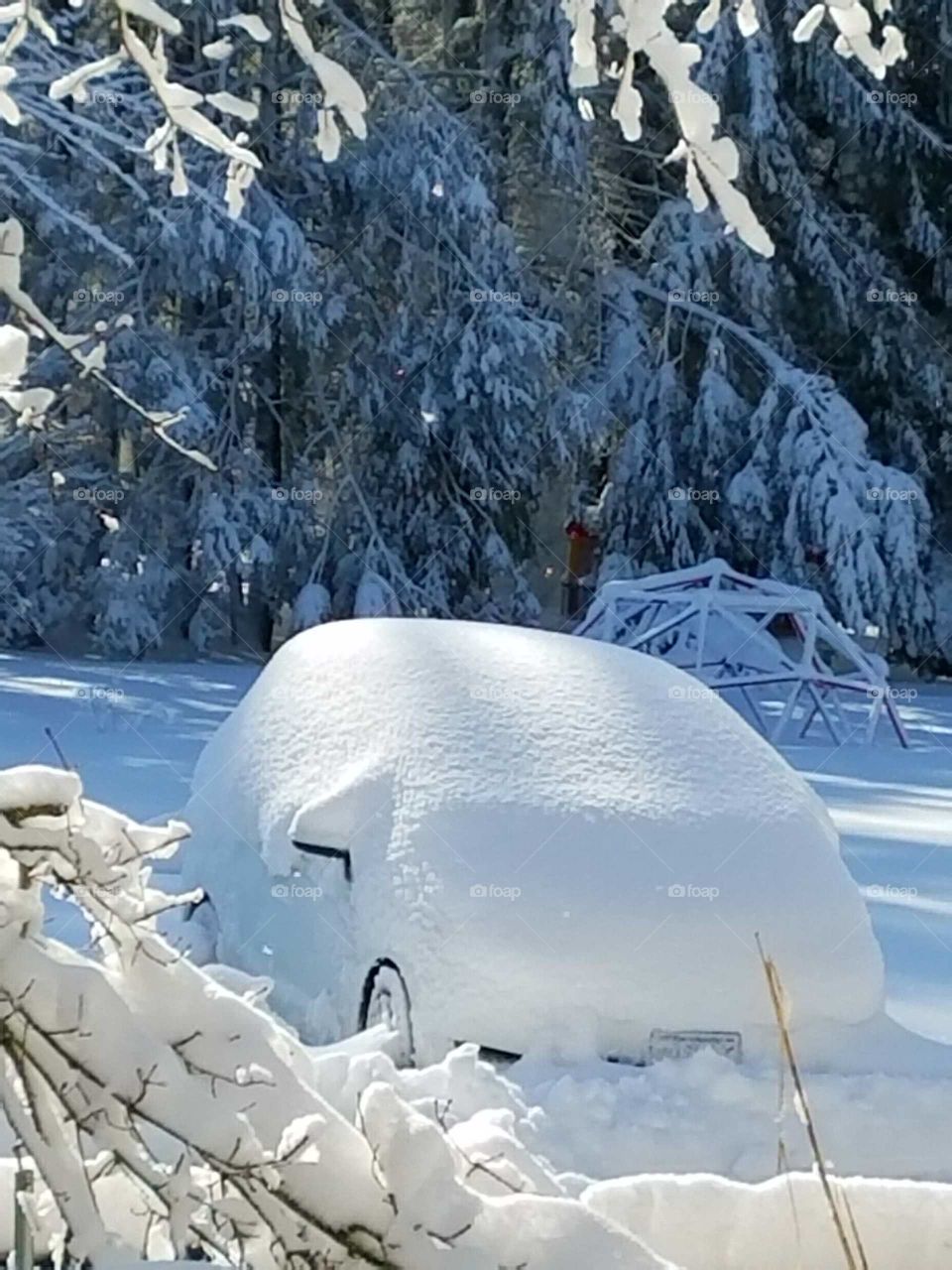 Car covered with icy snow after storm looking like a big snowball, one wheel showing.