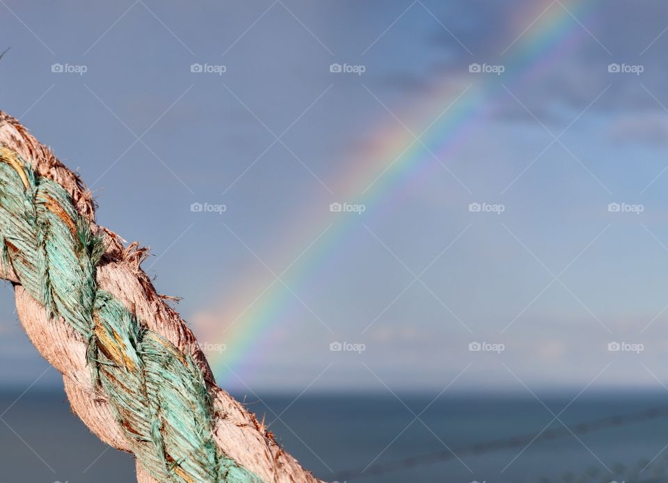 Colourful Nautical rope closeup foreground with rainbow over ocean background