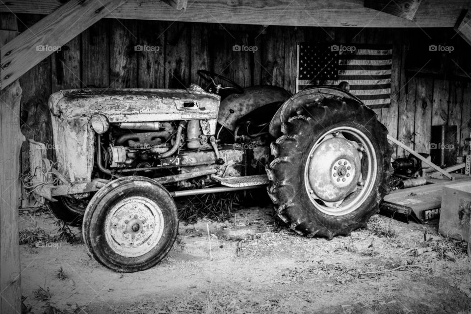 Black and white of an antique or vintage tractor in front of an American flag in an old barn. 