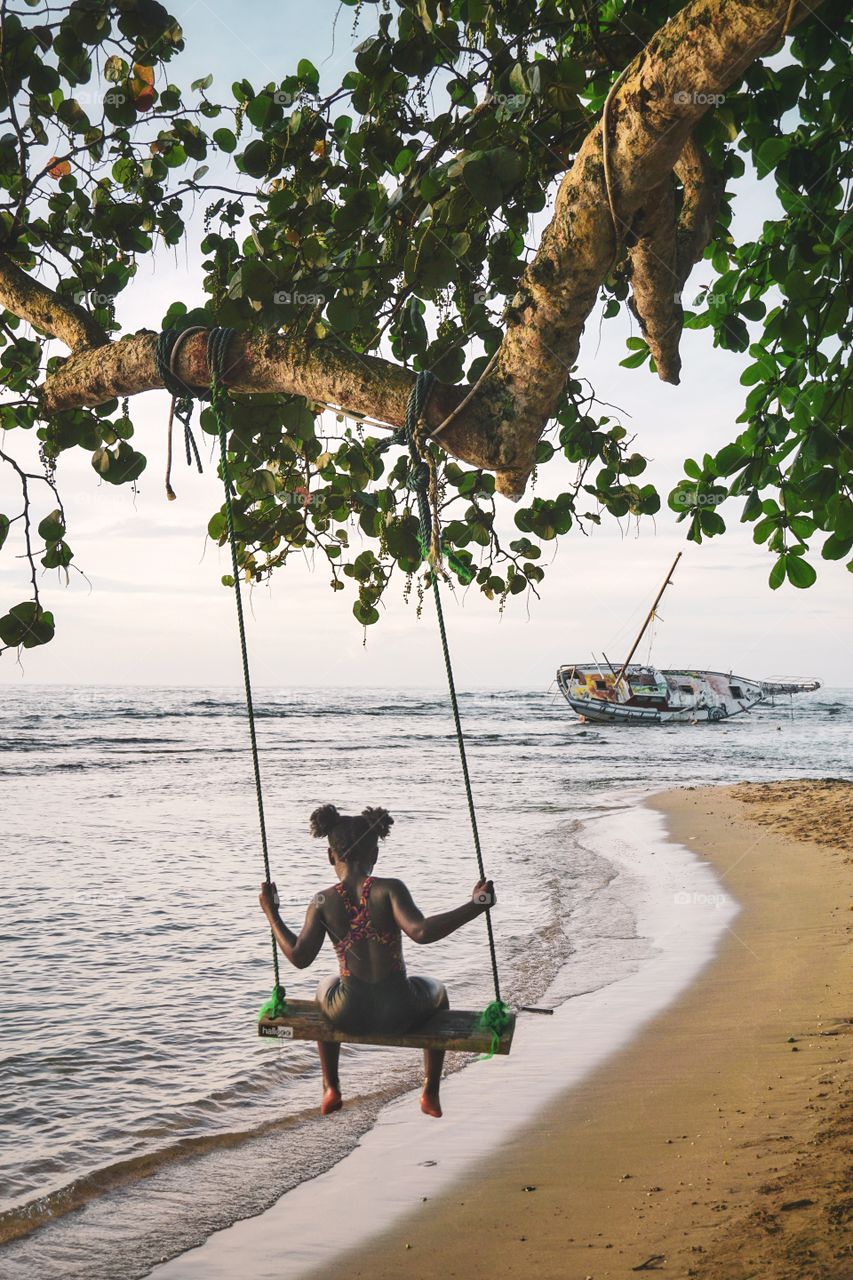 A girl on a wooden swing hanging from a tree