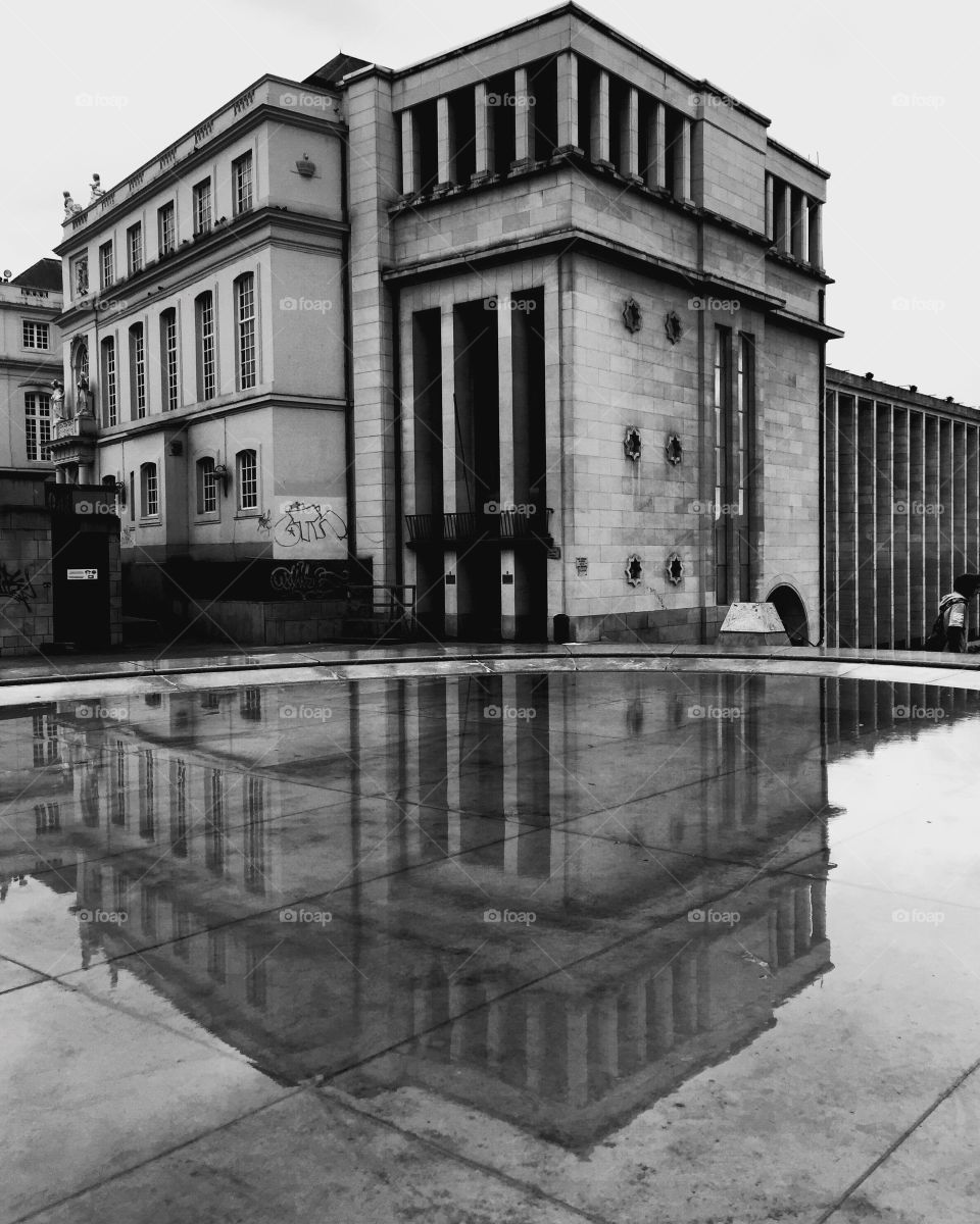 Black and white picture of a vintage building in the old city center of downtown Brussels reflected in the water of a fountain 
