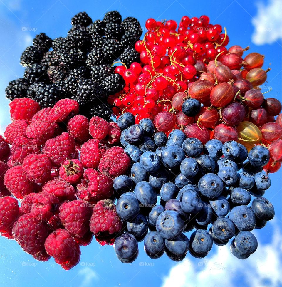 Explosion of color and taste. Berries on the mirror. Reflection of blue sky and white clouds