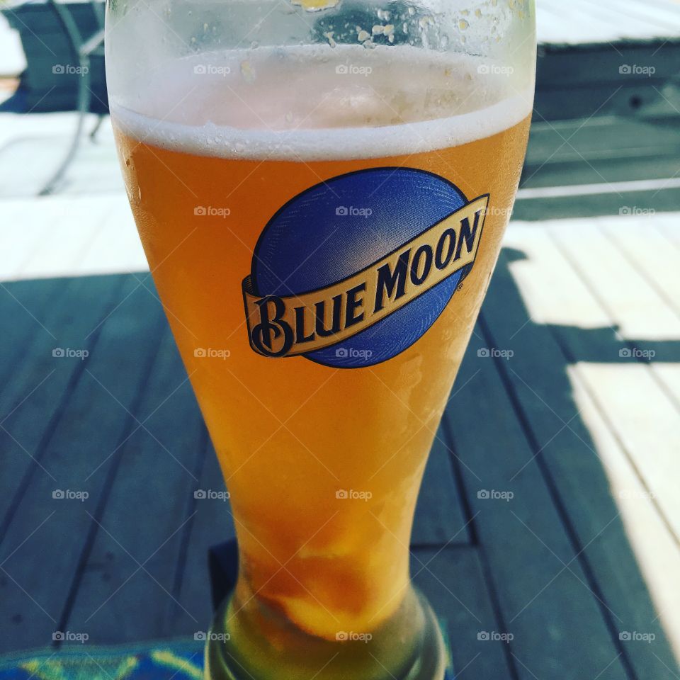 Tall glass of Blue Moon beer sitting outside on a beautiful sunny day